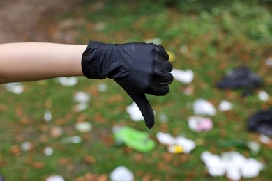 Woman showing thumb down in park, closeup. Garbage collection