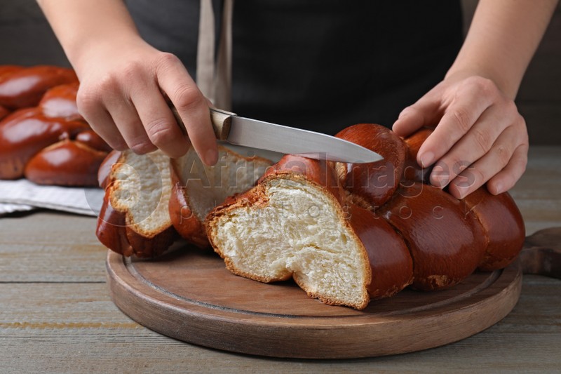 Photo of Woman cutting homemade braided bread at wooden table, closeup. Challah for Shabbat