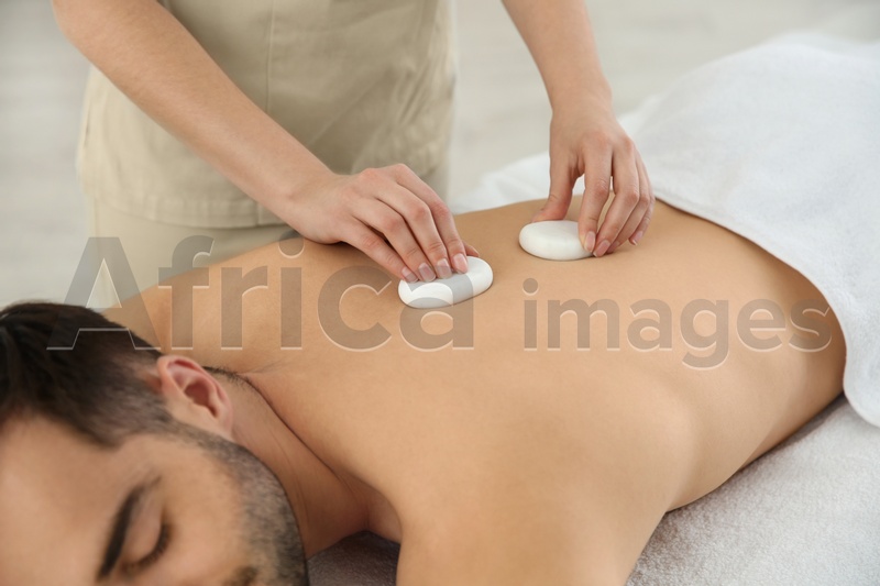 Photo of Man receiving hot stone massage in spa salon, closeup