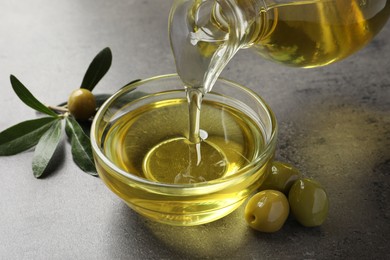 Pouring olive oil into glass bowl on grey table, closeup
