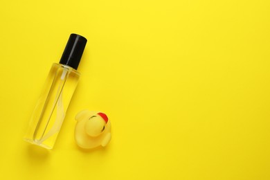 Bottle of baby oil and toy duck on yellow background, flat lay. Space for text