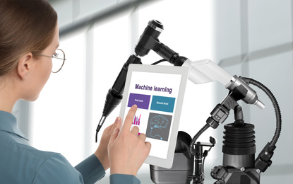 Engineer controlling electronic laboratory robot manipulator with tablet indoors. Machine learning