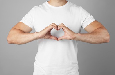 Man making heart with hands on grey background, closeup