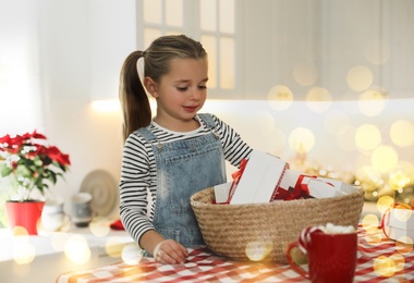 Image of Cute little girl taking gift from Christmas advent calendar at table in kitchen. Bokeh effect