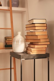 Stack of different books and vase on table near bookshelves in home library