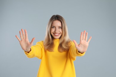 Woman showing number ten with her hands on light grey background