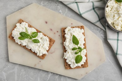 Photo of Crispy crackers with cottage cheese and basil on light grey marble table, flat lay