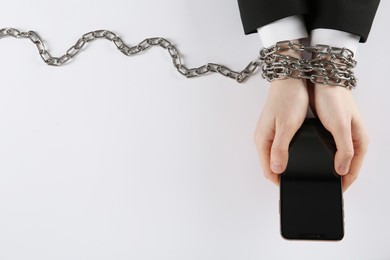 Man with chained hands holding smartphone on white background, top view. Internet addiction