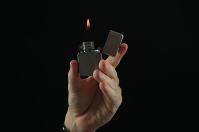 Man holding lighter with burning flame on black background, closeup