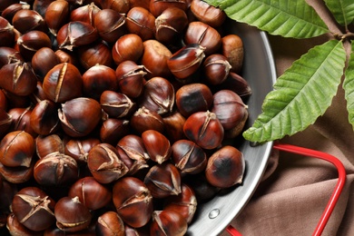 Delicious roasted edible chestnuts in frying pan on table, top view