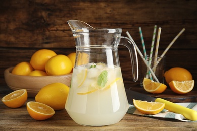 Cool freshly made lemonade in glass pitcher and fresh fruits on wooden table