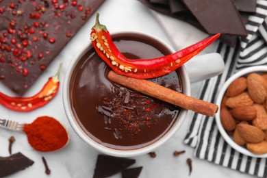 Photo of Cup of hot chocolate with chili pepper and cinnamon on white marble table, flat lay