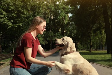 Cute golden retriever dog giving paw to young woman in park