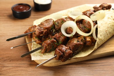 Metal skewers with delicious meat, tortilla and onion served on wooden table, closeup