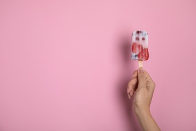 Woman holding berry popsicle on pink background, closeup. Space for text
