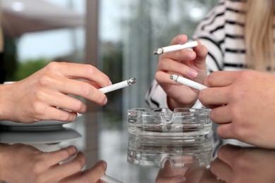 Women holding cigarette over glass ashtray at table, closeup