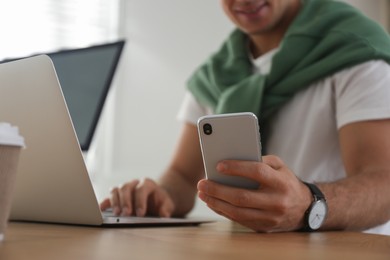 Freelancer working with laptop and smartphone at table indoors, closeup