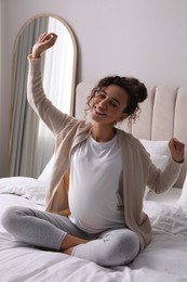 Excited pregnant young African-American woman sitting on bed at home