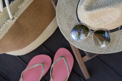 Stylish hat with sunglasses, bag and flip flops on wooden floor, above view. Beach accessories