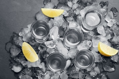 Shot glasses with vodka, ice and lemon on grey table, flat lay
