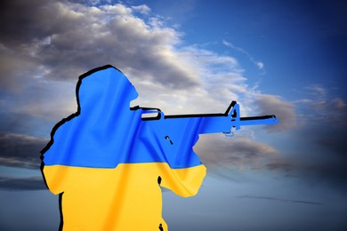 Silhouette of soldier in color of Ukrainian flag with assault rifle against cloudy sky