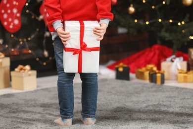 Photo of Little child holding gift box behind his back at home, closeup. Christmas celebration