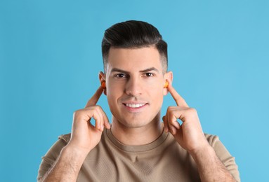 Man inserting foam ear plugs on light blue background
