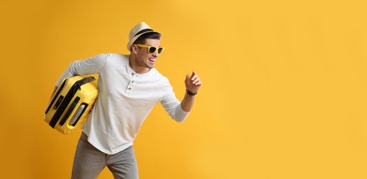 Male tourist with suitcase running on yellow background