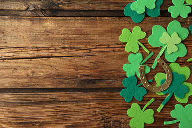 Flat lay composition with clover leaves and horseshoe on wooden background, space for text. St. Patrick's day