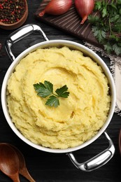 Photo of Pot of tasty mashed potatoes with parsley on black wooden table, flat lay