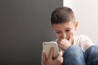 Upset boy with smartphone indoors. Space for text