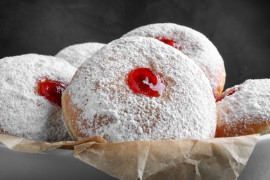 Delicious donuts with jelly and powdered sugar in bowl, closeup
