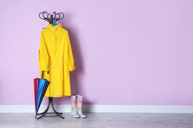Umbrella, raincoat and gumboots near color wall with space for design