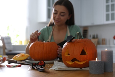 Woman making pumpkin jack o'lantern at table in kitchen. Halloween celebration
