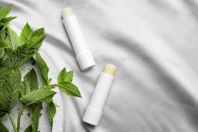 Hygienic lipsticks and mint leaves on light silk fabric, flat lay. Space for text