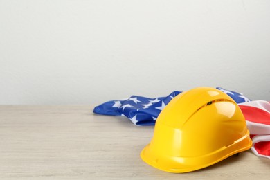 Yellow protective hard hat and American flag on white wooden table. Space for text