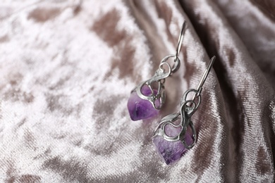 Beautiful pair of silver earrings with amethyst gemstones on light fabric, closeup