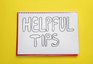 Phrase Helpful Tips in notebook on yellow background, top view