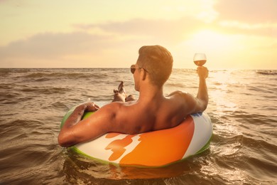 Man with glass of wine and inflatable ring resting in sea, back view