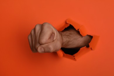 Man breaking through orange paper with fist, closeup