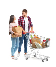Young couple with full shopping cart and paper bags on white background