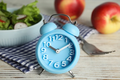 Alarm clock and healthy food on white wooden table, closeup. Meal timing concept