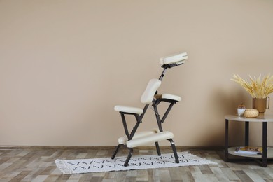Modern massage chair and table with decorative elements near beige wall indoors, space for text. Medical equipment