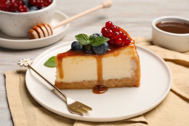 Photo of Slice of delicious cheesecake served with berries and caramel sauce on white wooden table, closeup