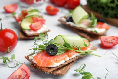 Tasty rye crispbreads with salmon, cream cheese and cucumber on light grey table, closeup