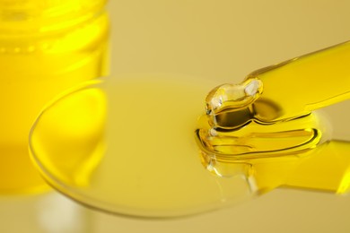 Dripping face serum from pipette on yellow background, closeup