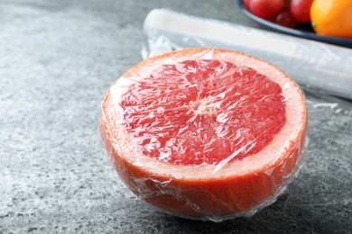 Half of grapefruit with plastic food wrap on grey table, closeup