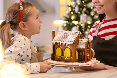 Mother and daughter with gingerbread house in kitchen, closeup