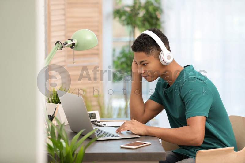 African-American teenage boy with headphones using laptop at table in room