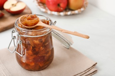 Delicious apple jam in jar and wooden spoon on table